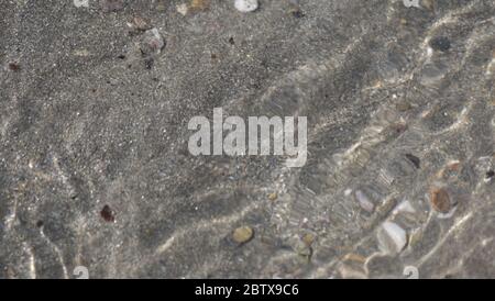 Sea water moving over a sandy beach on a warm sunny day Stock Photo