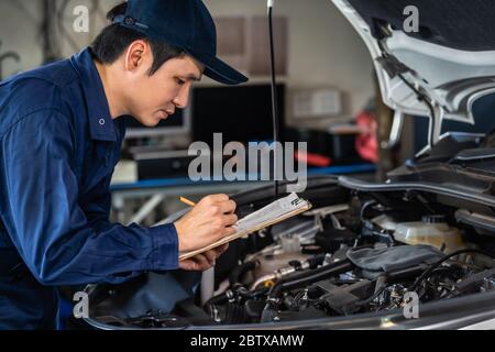 male mechanic checking and repair service a car with clipboard Stock Photo