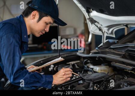 male mechanic checking and repair service a car with clipboard Stock Photo