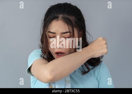 sick young woman is coughing into her sleeve or elbow to prevent spread Covid-19, Corona virus Stock Photo