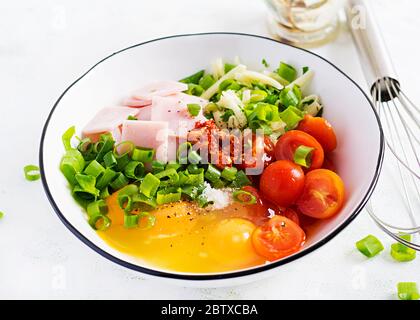 Omelette ingredients: eggs, ham, tomatoes, green herbs, milk and cheese on the light table. Stock Photo