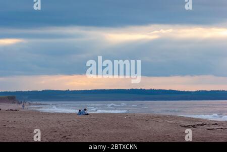 Sunset at Cavendish Beach, PEI National Park, Canada. Couple enjoying a relaxing evening. Sunbeam shining through an opening in the clouds. Stock Photo