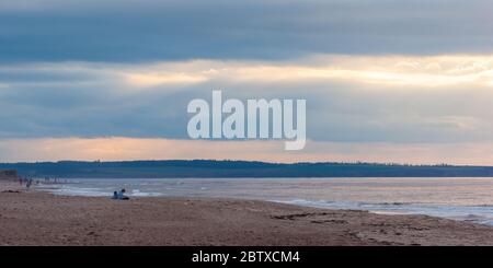 Sunset at Cavendish Beach, PEI National Park, Canada. Couple enjoying a relaxing evening. Sunbeam shining through an opening in the clouds. Stock Photo