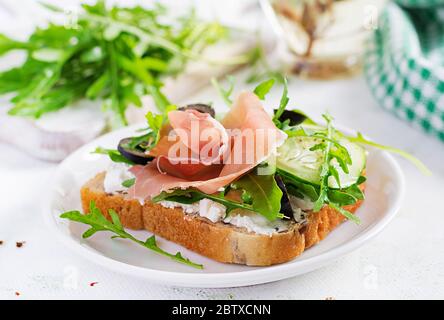 Sandwich with prosciutto, cucumber, black olives, arugula and feta cheese on  table.  Trend food. Stock Photo