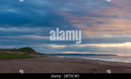 Dramatic sunset at Cavendish Beach, PEI National Park, Canada. Couple enjoying a relaxing evening. Sunbeam shining through an opening in the clouds. Stock Photo