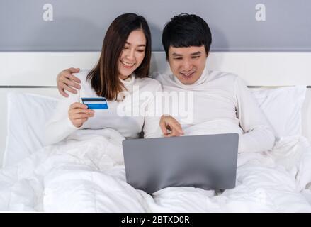 couple using laptop computer to shopping online with credit card on a bed Stock Photo