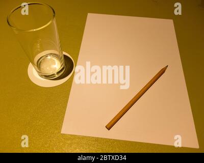 On the table are a glass of A4 paper water and brown wooden pencils. Stock Photo