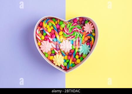 mix colorful chocolate sweets lie in gift box shape of heart on colorful background Flat lay Top view Stock Photo