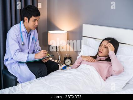 doctor talking and writing the diagnosis on clipboard with female patient on a bed Stock Photo