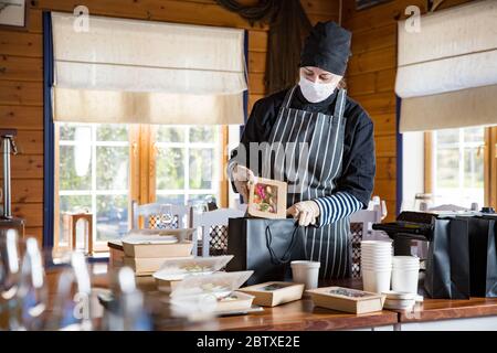 Restaurant worker wearing protective mask and gloves packing food boxed take away. Food delivery services and Online contactless food shopping. Stock Photo