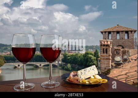 Two glasses of wine with charcuterie assortment on view of Verona, Italy. Glass of red wine with different snacks - plate with ham, sliced, blue chees Stock Photo