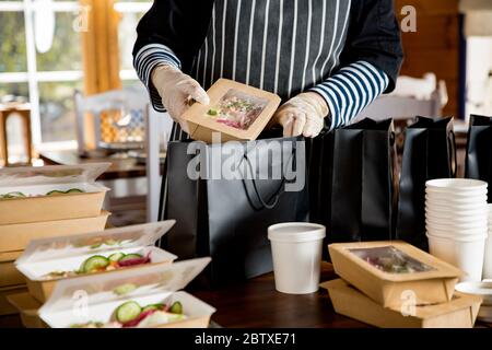 Restaurant worker wearing protective mask and gloves packing food boxed take away. Food delivery services and Online contactless food shopping. Stock Photo