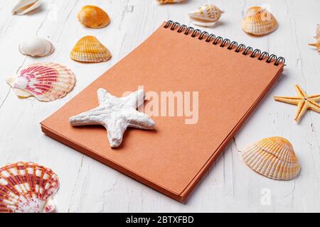 Brown open notepad surrounded by sea shells on white wooden table closeup Stock Photo