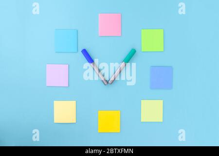 Clock made of colorful stickers and markers on blue background. Copy space, flat lay. Concept office and back to school. Stock Photo