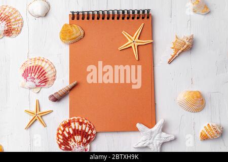 Brown open notepad surrounded by sea shells on white wooden table closeup Stock Photo
