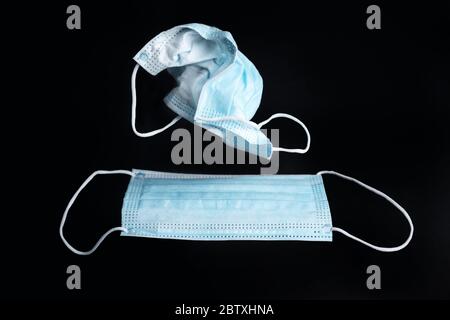Old and new face mask isolated on black background. Used surgical mask above new one on dark backdrop Stock Photo