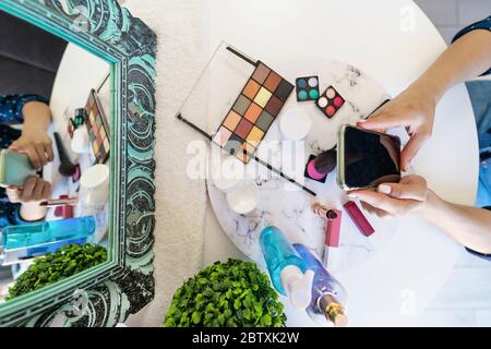 Top view young woman using mobile smartphone while doing makeup at home - Beauty cosmetic industry and technology addicted people concept Stock Photo