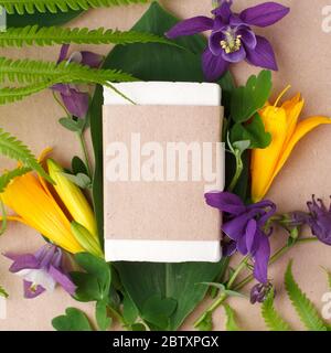 Hand made white coconut oil soap in craft paper, plants and flowers on craft paper background, skincare product, hand hygiene, herbal soap bar in pape Stock Photo