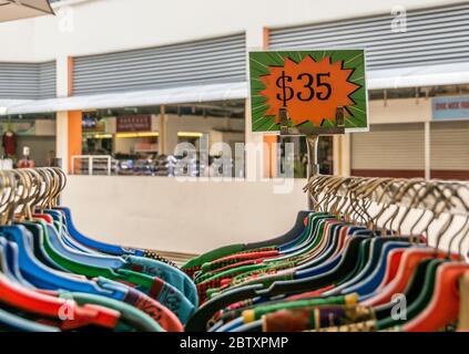 A clear sign, advertising the sales price of a rack of clothes on very colourful hangers Stock Photo