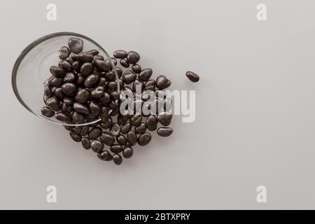 raisins in chocolate in a glass bowl pour out on a glossy light surface Stock Photo