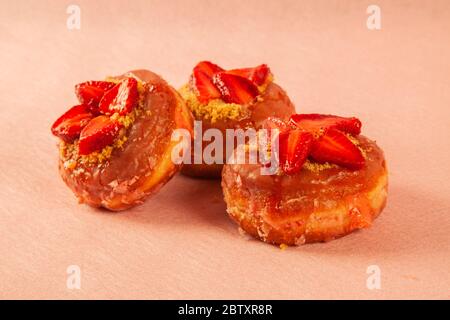 Three strawberry shortcake donut on a pink coloured background Stock Photo