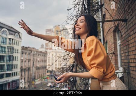 Cheerful lady standing on balcony and greeting friend