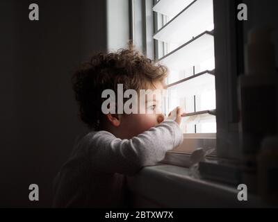 Two year old toddler looks out of the window Stock Photo