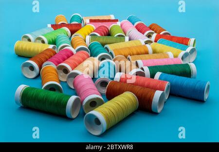 Spools of sewing thread in many colors on a blue background. Stock Photo