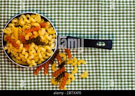 Small mini frying pan with tricolor raw fusilli pasta in a rustic composition. Stock Photo