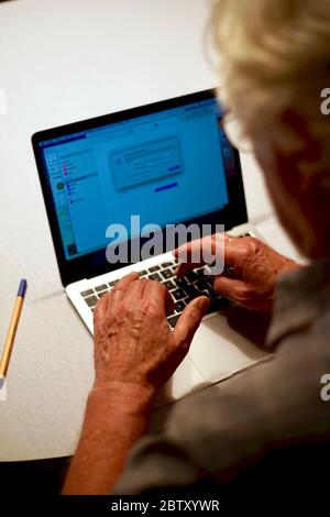 Over shoulder back view of white haired retired senior man using laptop computer at home. Stock Photo