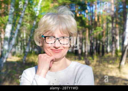 Portrait of a happy middle-aged woman with glasses walking in the park. Bright sunny summer day. The concept of freedom and joy. Stock Photo