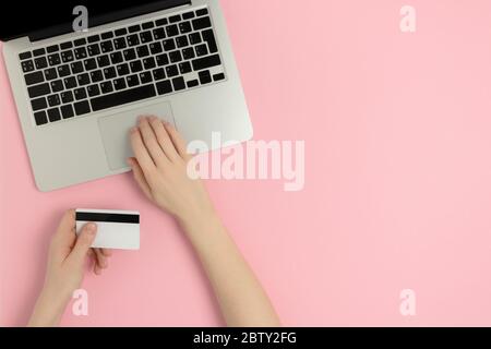 Female hands typing on laptop and hold credit card. Online shopping concept on a pink pastel background with copy space. Stock Photo