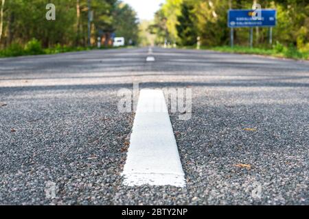 On the road. Low angle view of road with shallow depth of forest. Asphalt road closeup with white line on center Stock Photo