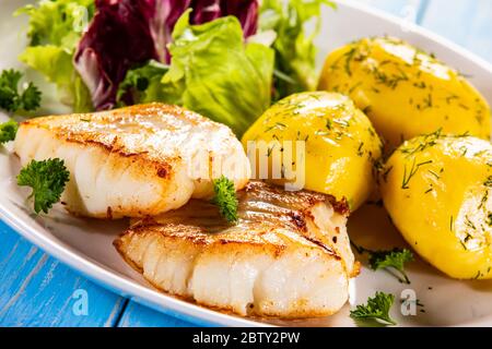 Fried fish with potatoes and vegetable salad on wooden table Stock Photo