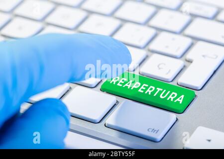 Reopening word in spanish language on green key Keyboard. Coronavirus Covid-19 pandemic. Hand with protective glove ready to push the button Stock Photo