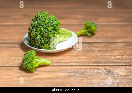 green broccoli on a white plate and pieces of broccoli on the wood Stock Photo