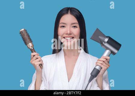 Brunette young asian woman holding a brush and a hair dryer Stock Photo