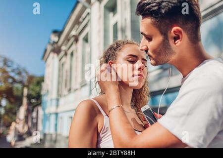 Mixed race couple in love listening to the music in city. Arab man puts earphone into girlfriend's ear on street Stock Photo