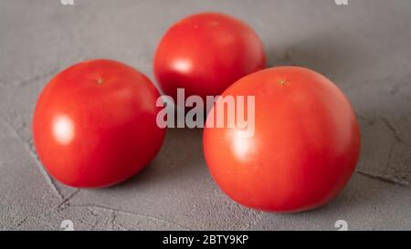 Close up three isolated tomatoes on concrete background. Fresh and healthy food good for your eyes, heart and kidneys. Stock Photo