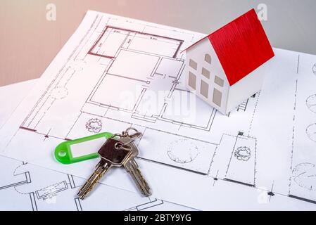 Model house and keys lying on house blueprints on a desk. Real estate and construction industry concept. Stock Photo