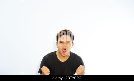 Happy winner. Happy young handsome Asian man gesturing and keeping mouth open while standing against white background Stock Photo