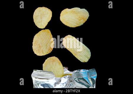 potato chip falling to aluminium foil packaging on black background Stock Photo