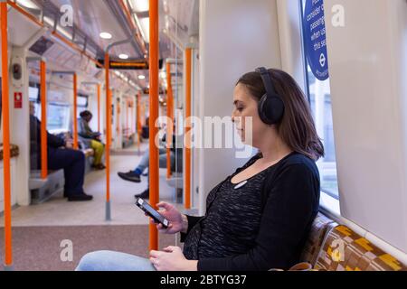 A pregnant commuter sitting in a priority seat on a London Overground train. Stock Photo