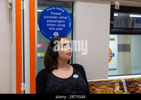 A pregnant commuter sitting in a priority seat on a London Overground train. Stock Photo