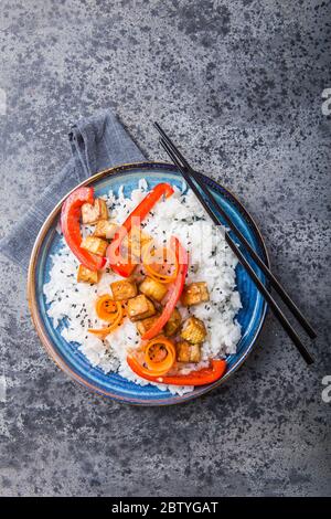 Vegan tofu poke bowl with rice, pepper, carrot and cumin in a ceramic bowl, gray background. Stock Photo