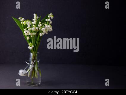 A bouquet of lilies of the valley on a black background with place for text. Delicate white spring flowers. Bouquet in a glass bottle. Copyspace. Stock Photo