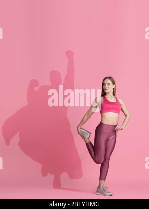 Superhero in shadow of ordinary people - modern superhero's concept, respect and admiration. Young woman stays active, sportive setting good example. Inspiring others to be strong and healthy. Stock Photo