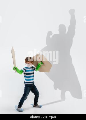 Superhero in shadow of ordinary people - modern superhero's concept, respect and admiration. Boy with sword keep fighting with coronavirus like warrior, setting good example. Inspiring others. Stock Photo