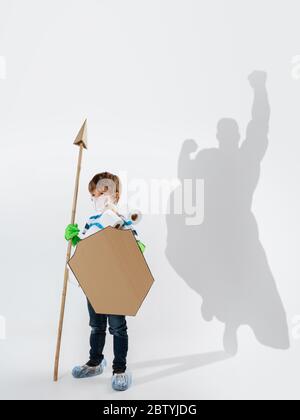 Superhero in shadow of ordinary people - modern superhero's concept, respect and admiration. Boy with sword keep fighting with coronavirus like warrior, setting good example. Inspiring others. Stock Photo