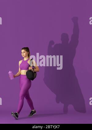 Superhero in shadow of ordinary people - modern superhero's concept, respect and admiration. Young woman stays active, sportive setting good example. Inspiring others to be strong and healthy. Stock Photo